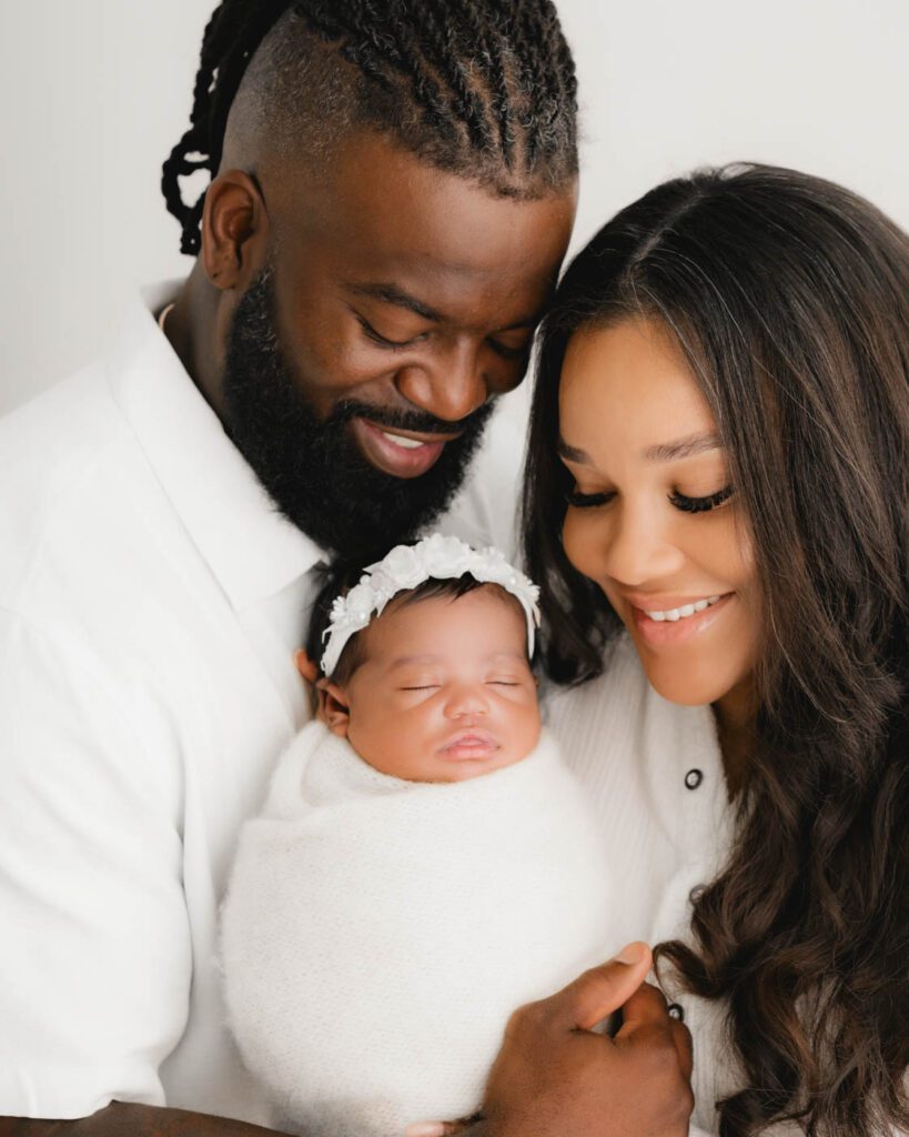 Parents Holding Their Newborn During A Professional Newborn Photography Session At A Dallas Photography Studio With Soft Studio Lighting.