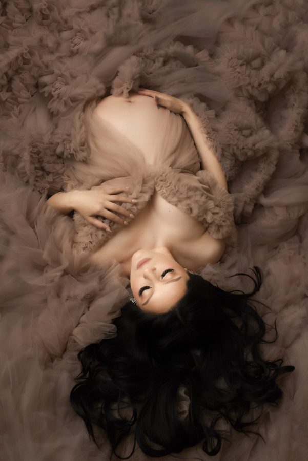 A pregnant woman laying on a bed of brown feathers.