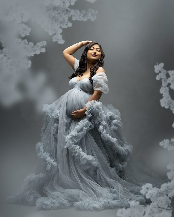 A pregnant woman is posing in a gray gown.