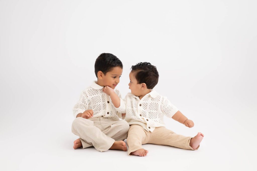 Why Include Siblings In Your Cake Smash Session? 17 Older Brother Sitting Beside His Baby Sibling Before Their Cake Smash Photography Session In Dallas