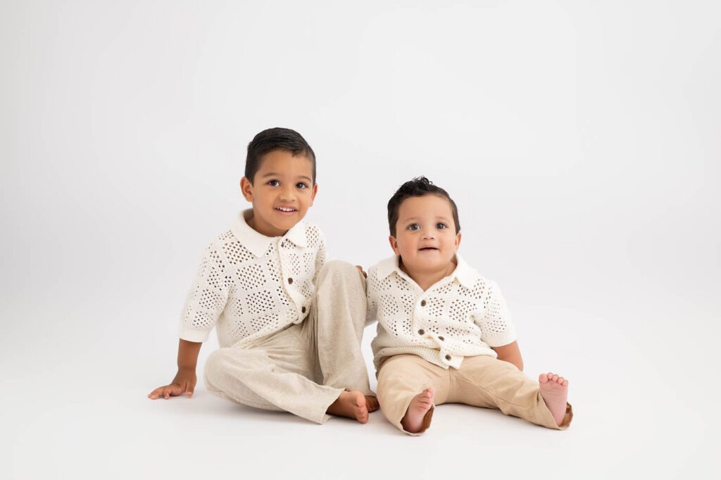 Why Include Siblings In Your Cake Smash Session? 15 Older Sibling Smiling Beside One-Year-Old Brother During First Birthday Portrait Session.