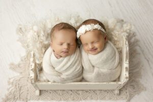 Photographing Twins Swaddled And Sleeping In A Miniature Wooden Bed With White, Fluffy Bedding.
