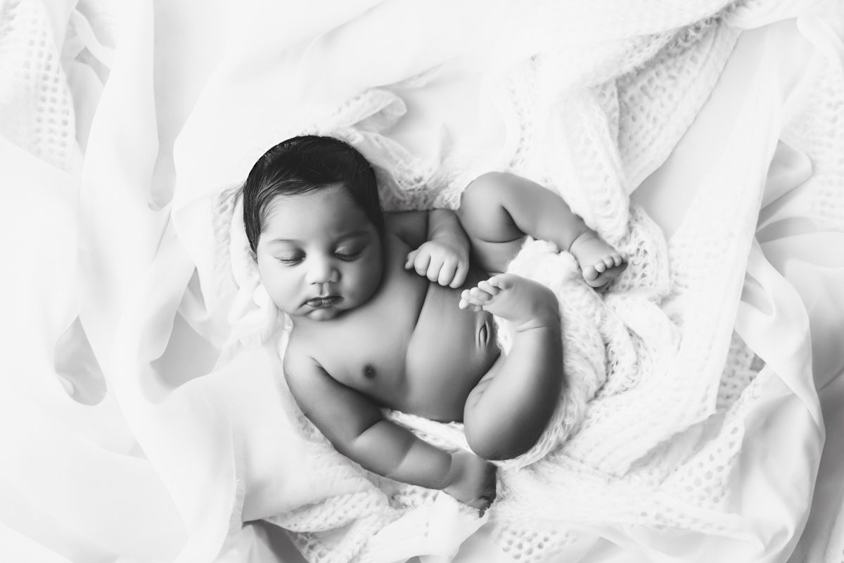 A newborn baby resting peacefully, wrapped in a soft, white knit blanket.