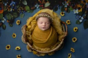 Newborn Baby Swaddled In A Mustard Yellow Blanket, Resting In A Basket Adorned With Sunflowers Creating An Ideal Scene For How To Budget For A Newborn Photoshoot