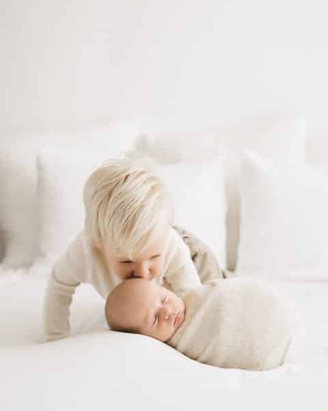 A Toddler Gently Kisses A Newborn Baby Wrapped In A Beige Blanket Perfect For Capturing, Role Of A Newborn Photographer For Birth Announcement 