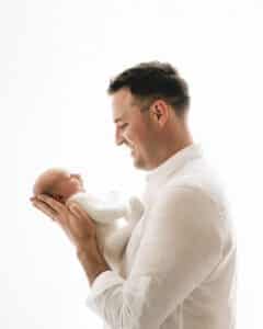 Father Holds A Newborn Baby In His Hands While Smiling, Perfectly Capturing Precious Moments Of Photography For Newborns