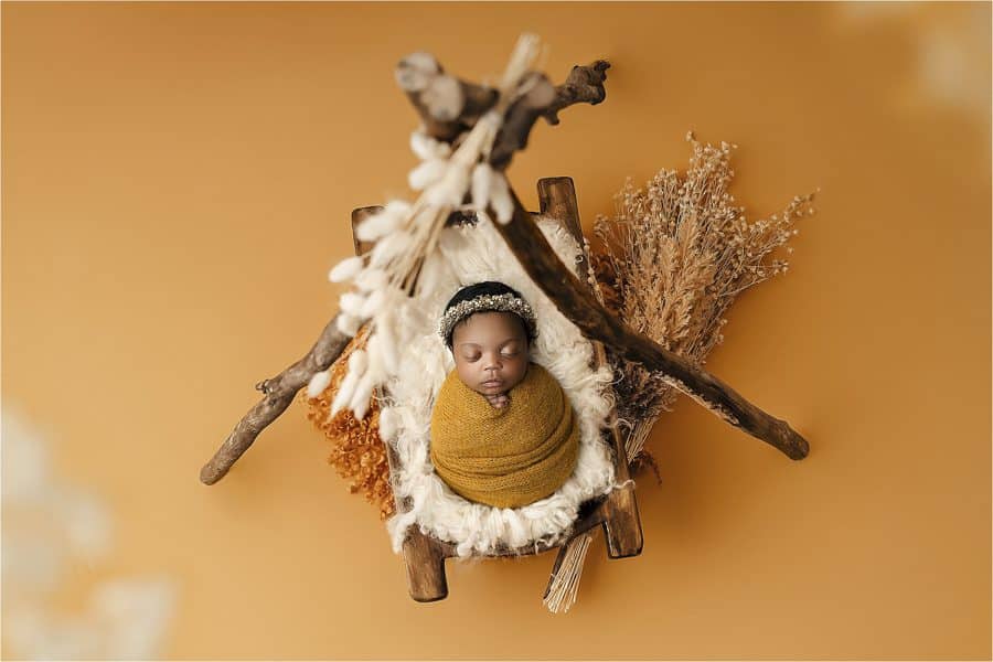 newborn cushioned on wooden bed with floral orange background for newborn photography