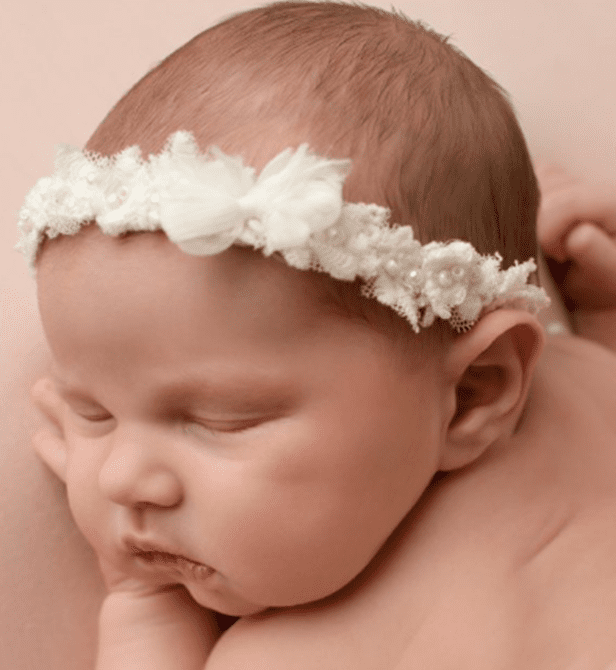 A Sleeping Baby, Adorned With A White Lace Headband With Floral Decorations, Rests Their Cheek On A Surface, Capturing The Charm Of The Little One In An Artistic Way.