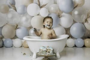 Baby Boy Smiling In A Tub For A Blue Balloon Themed Cake Smash Photoshoot | Pricing For Dallas Cake Smash Photography