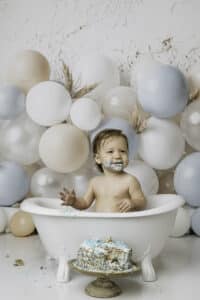 Baby Boy Sitting In A White Tub With Water Smiling During A Cake Smash Photoshoot | Pricing For Dallas Cake Smash Photography