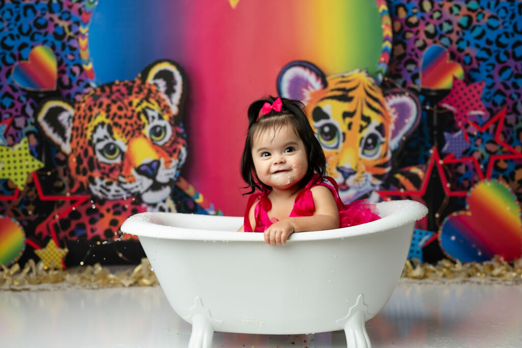 Baby Girl Smiling In White Tub During Colorful Cake Smash Milk Bath Session In Dallas