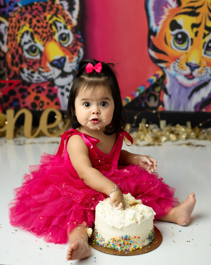 Rainbow Themed Lisa Frank Cake Smash Photoshoot In Plano Featuring Baby Girl Beside Birthday Cake