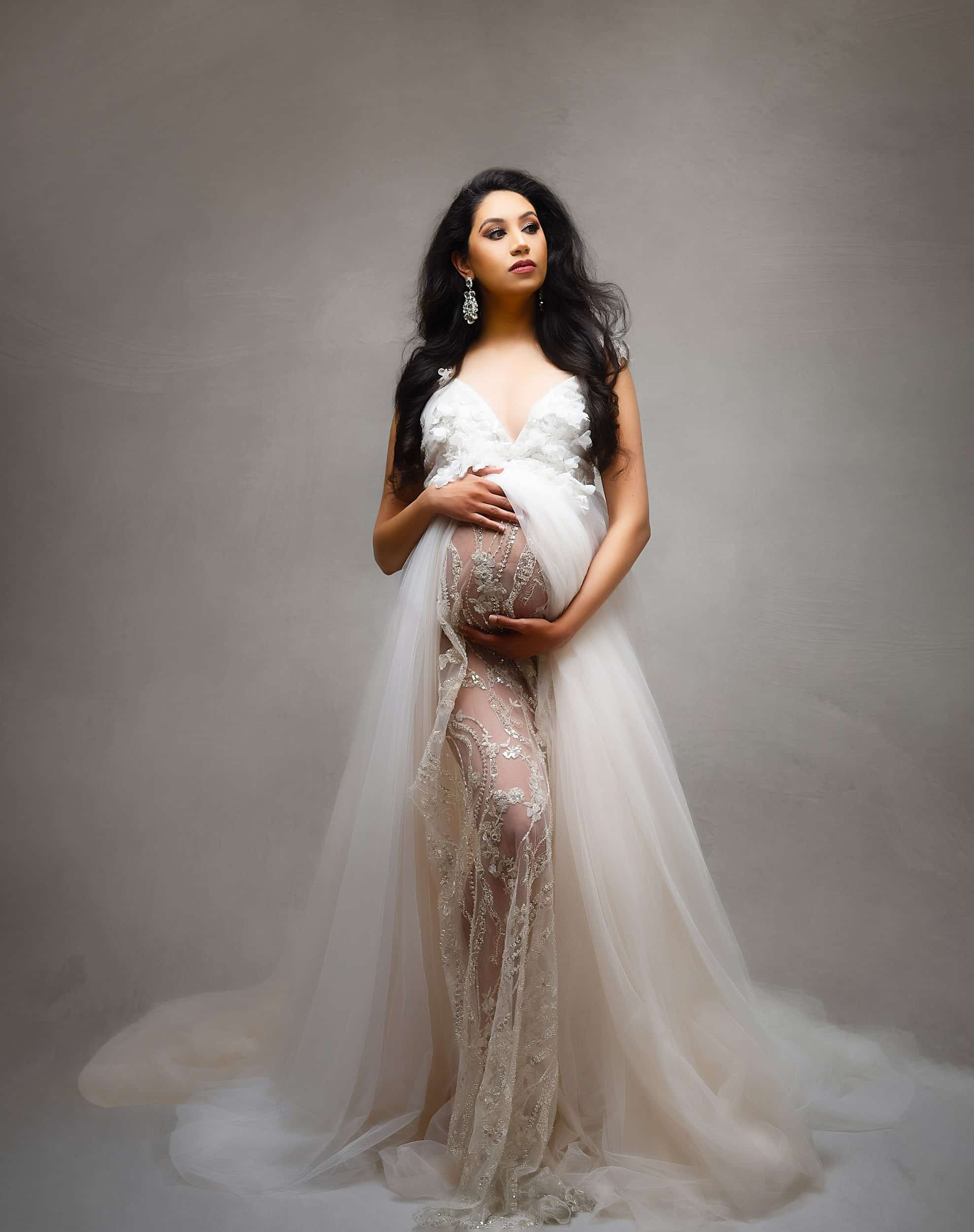 pregnant woman in a flowing white gown holding her belly with both hands for dallas maternity photographer | lily hayes photography