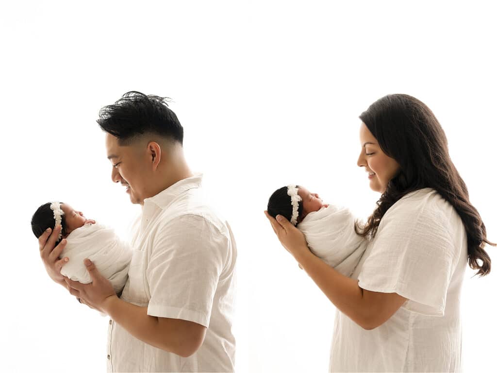 A Man And A Woman, Both Wearing White Shirts, Each Hold A Newborn Baby Wrapped In A White Blanket And Sporting A Headband, Set Against A White Background In Their Dallas Home. This Cozy Scene Captures The Essence Of Lifestyle Newborn Pictures.