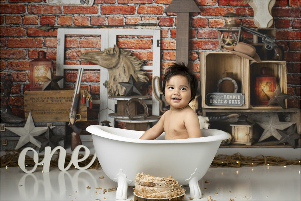 A Baby Sits In A Small White Tub With A Western-Themed Backdrop, Including A Cake In Front And The Word &Quot;One&Quot; Next To Them, Perfectly Capturing The Charm Of A Cowboy Cake Smash. This Delightful Moment Was Expertly Shot By A Talented Dfw Photographer.