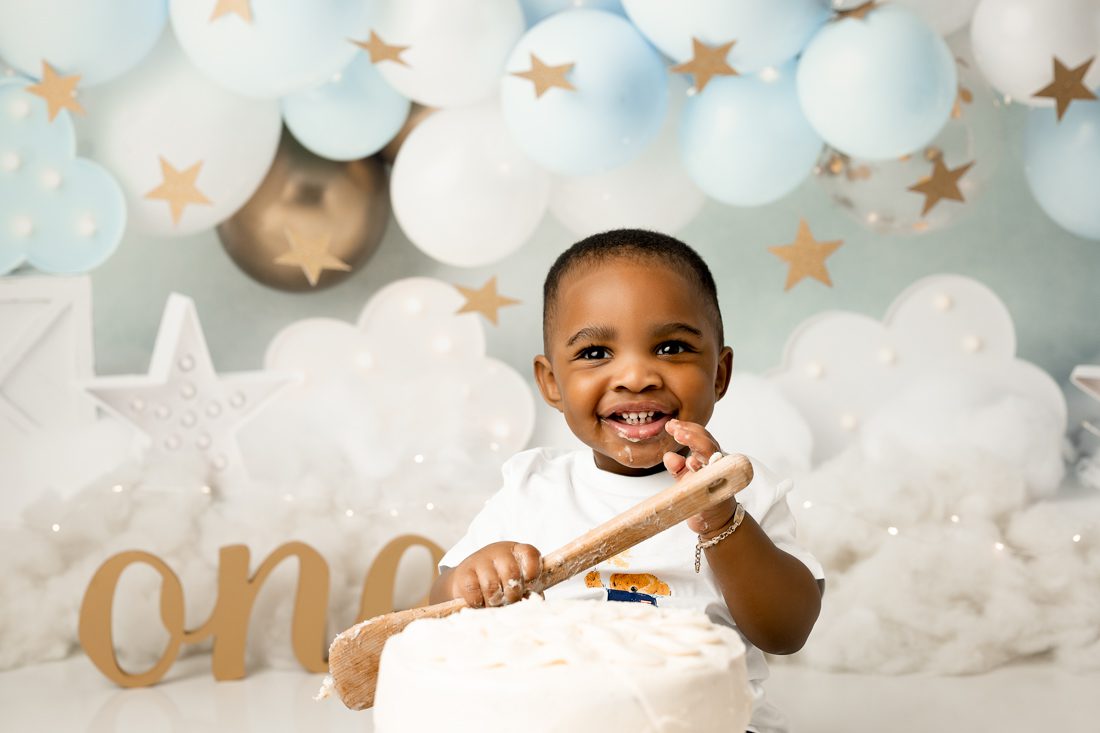 Baby Holding Spoon Smiling While Eating Cake For Cake Smash Photography Dallas