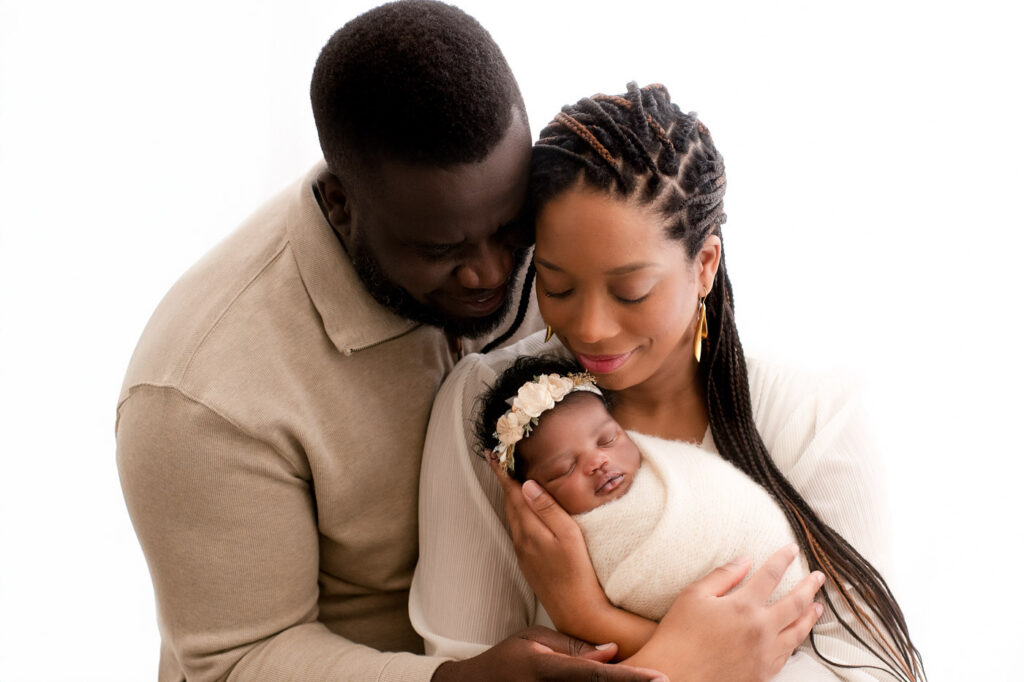 Lifestyle Newborn Photography In Dallas Featuring Parents Holding Their Newborn Baby In A Soft, Neutral Studio Setting