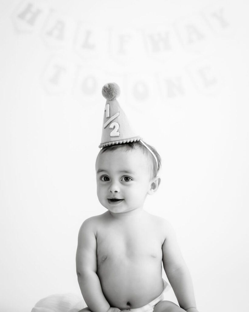 Black And White Diy Birthday Portrait Of A Baby Wearing A Party Hat With A Neutral Backdrop