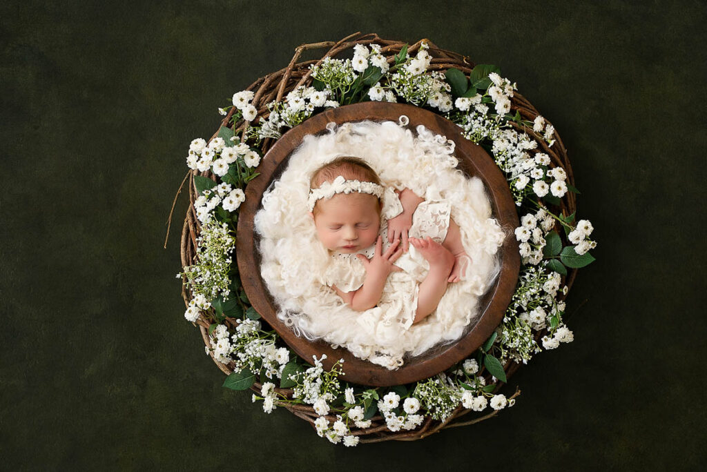 How To Start A Newborn Photography Portfolio 9 Newborn Styled In A Rustic Bowl Surrounded By White Florals Against A Dark Background