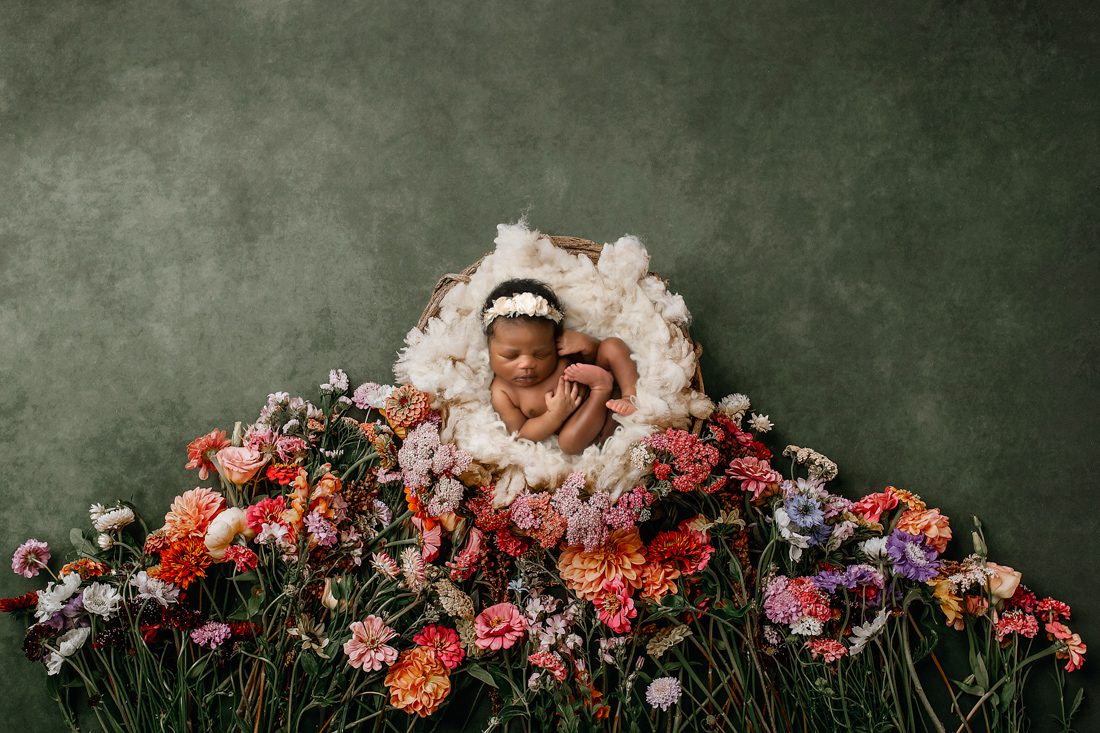 baby rests peacefully in a basket surrounded by floral for dallas newborn photographer