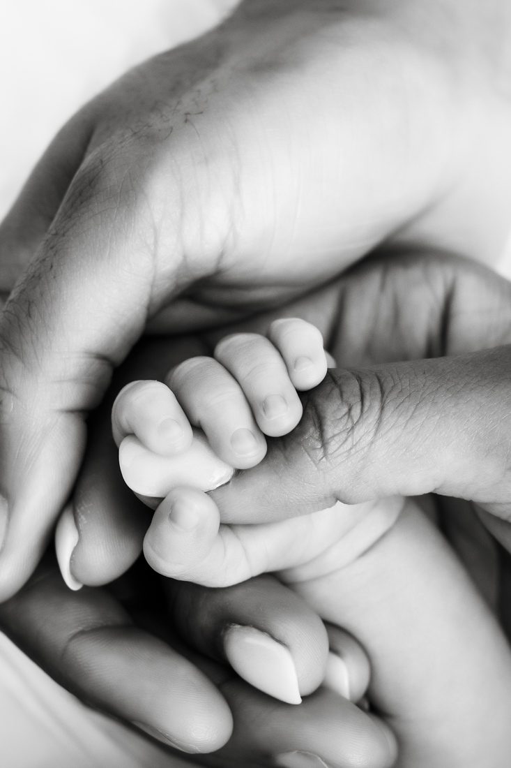 Newborn Lifestyle Photographer Captures Intimate Black And White Photo Of Father Holding Newborn Hand