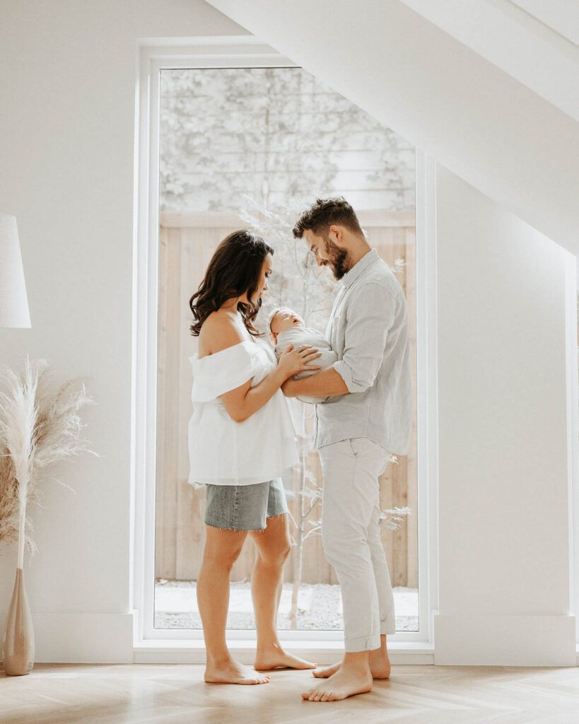 Parents Holding Newborn In Bright Home During Lifestyle Newborn Session