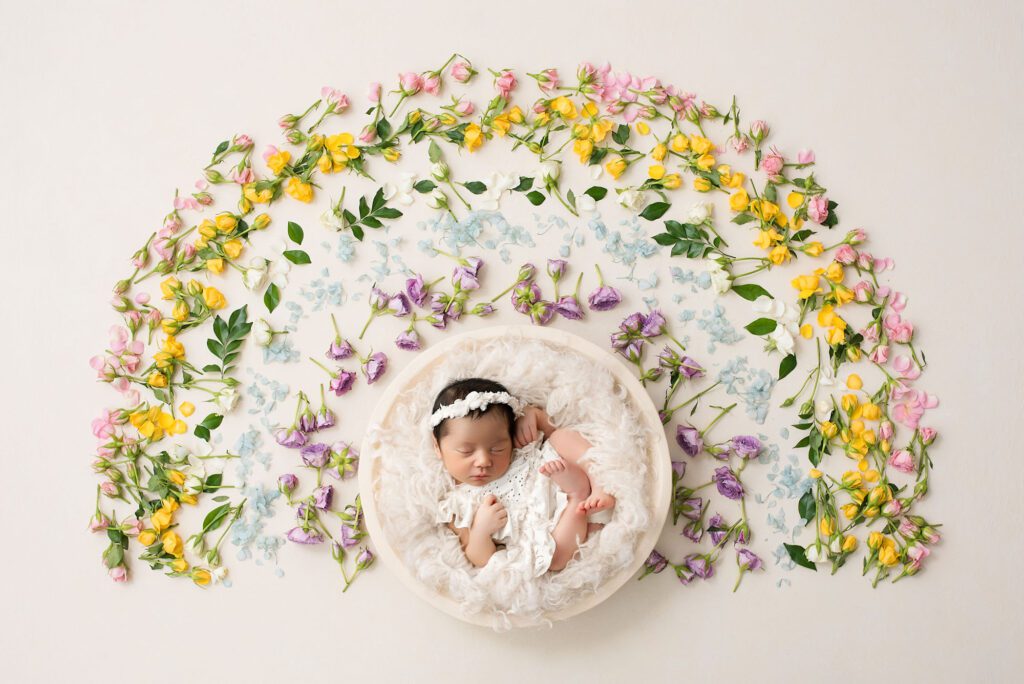 Newborn Baby Girl Sleeping In A Round Bowl With A Floral Headband, Surrounded By Colorful Flower Circle – Newborn Session Color Scheme Dallas