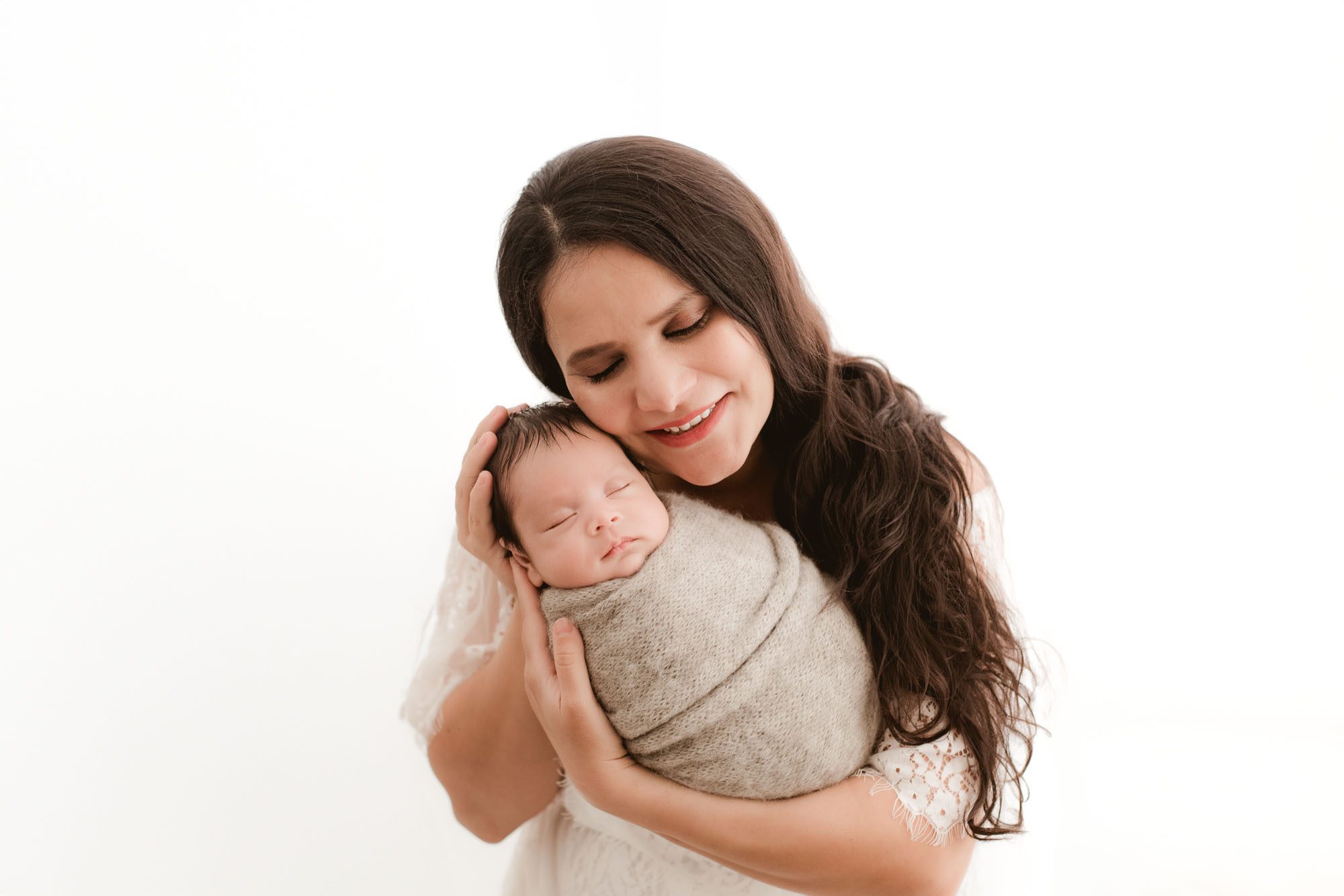 Dallas newborn photographer captures mother smiling while holding swaddled baby