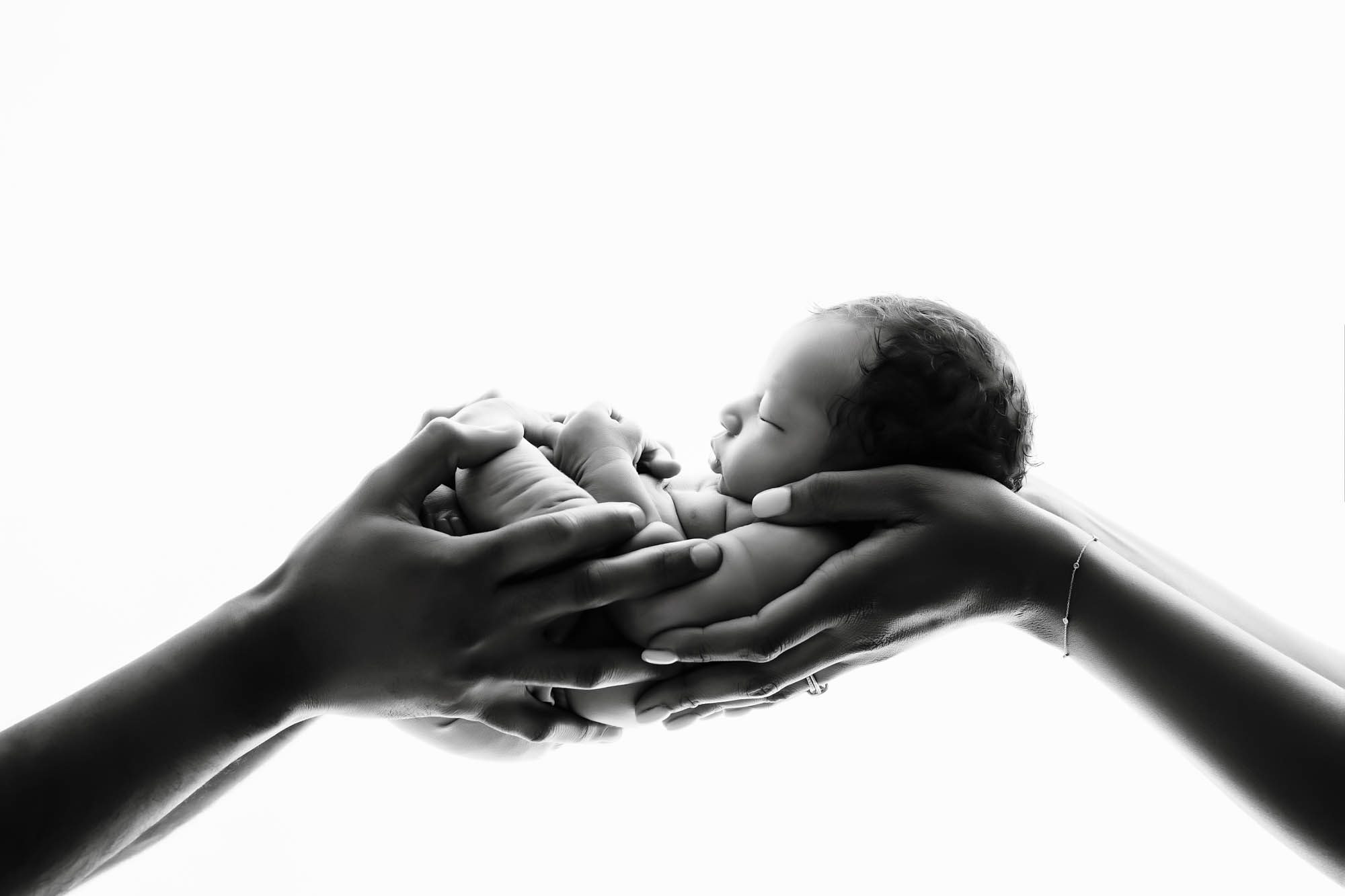 Black and white newborn lifestyle newborn photographer of baby held safely in parents' hands in Dallas studio.