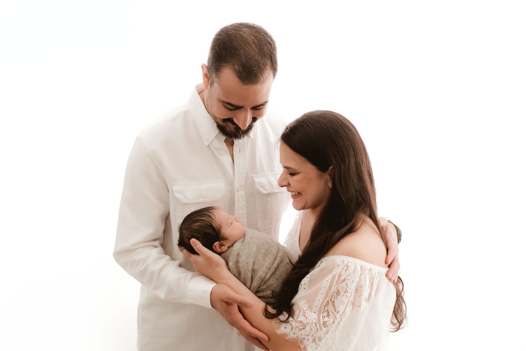 Dallas family newborn photography captures parents smiling at their swaddled baby