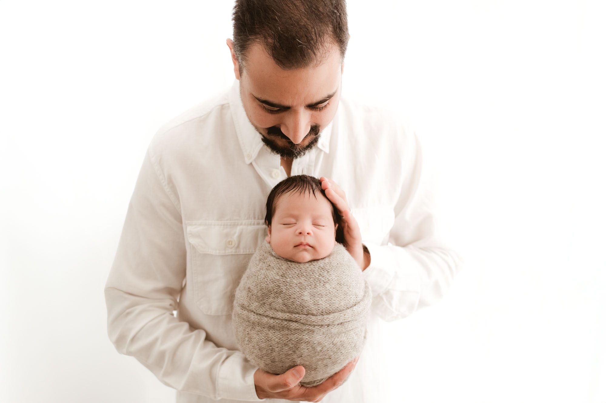 Newborn Photography In Dallas With Father Looking Down At Swaddled Baby