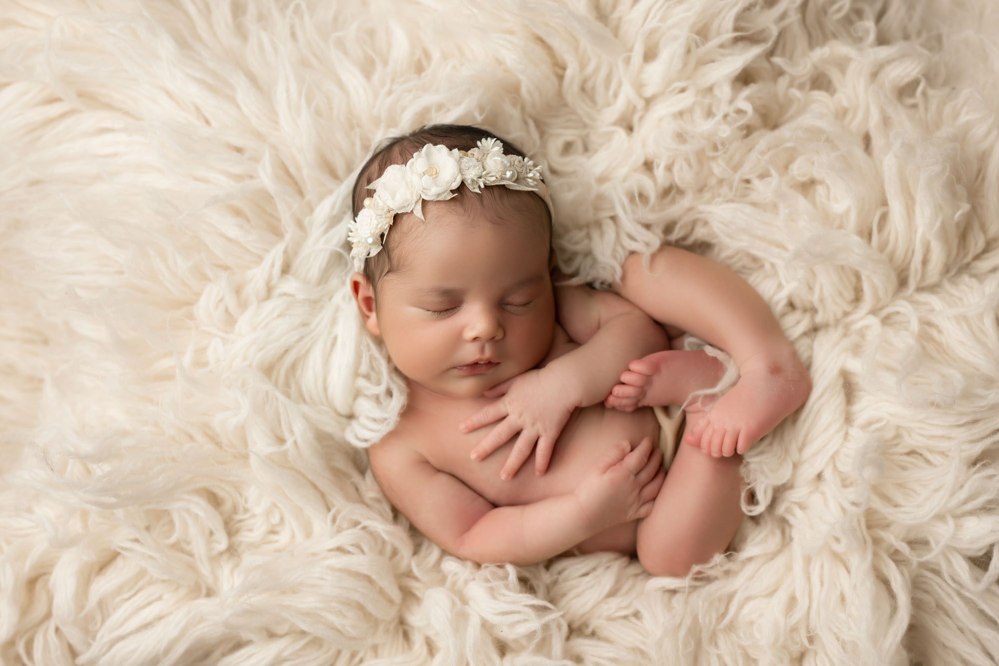 Newborn Baby Girl Sleeping Peacefully On Cream Fluffy Blanket, Wearing Floral Headband – Dallas Newborn Photographer