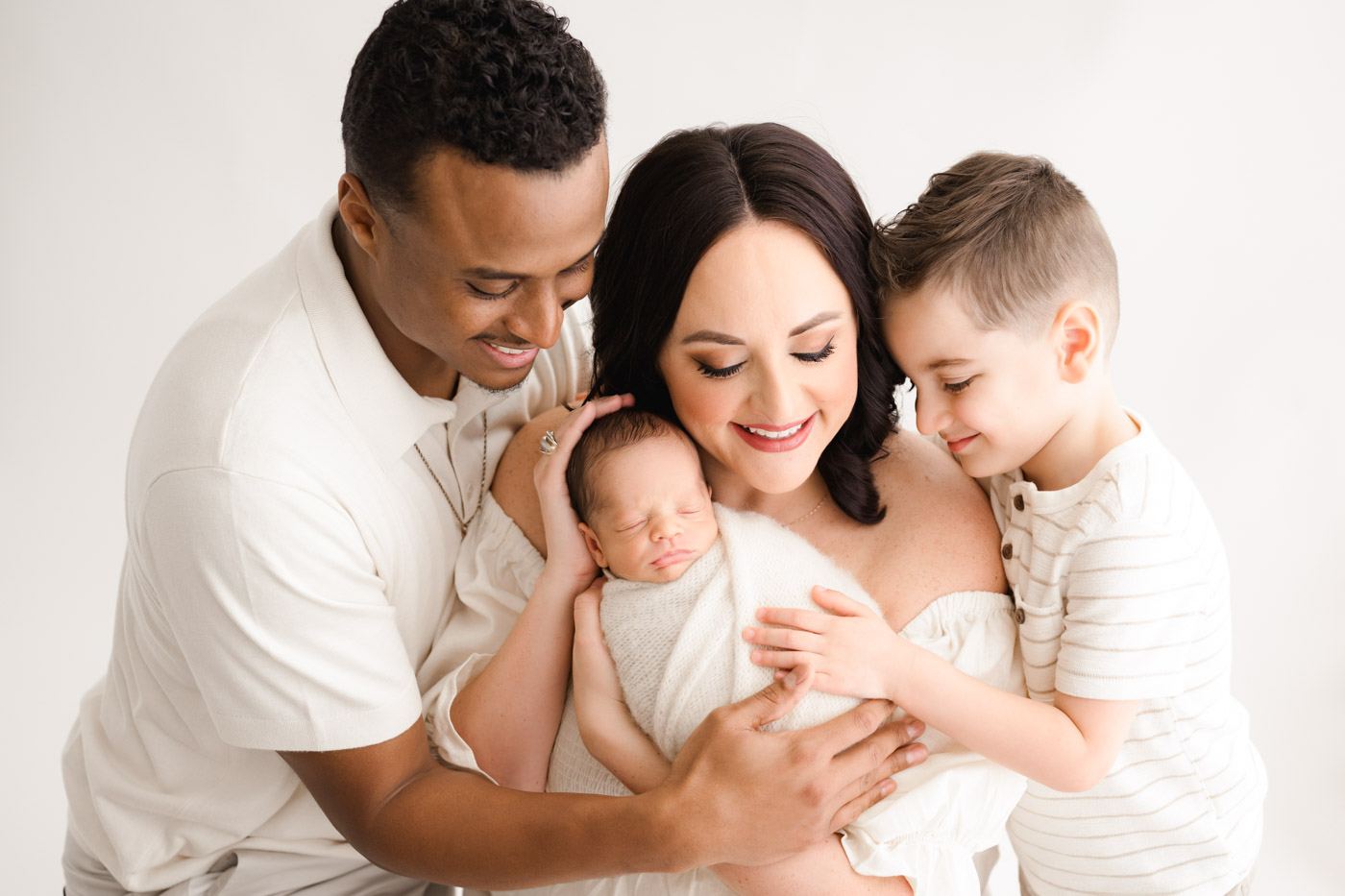Dallas Newborn Photography Family Portrait With Parents And Sibling Holding Baby In Soft Neutral Studio Setting