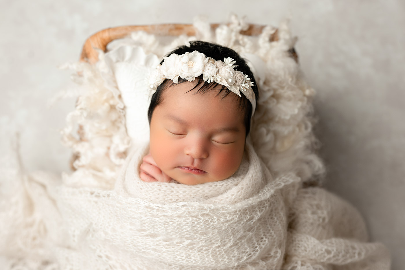 Newborn Baby Wrapped In Soft Neutral Fabrics Resting On Textured Backdrop In Dallas Studio