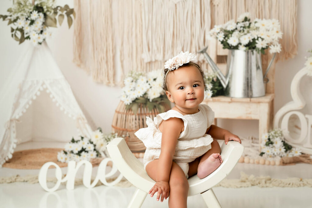 Baby Girl Sitting On A White Crescent Moon Prop During A Neutral Boho Cake Smash Photography Session In Dallas