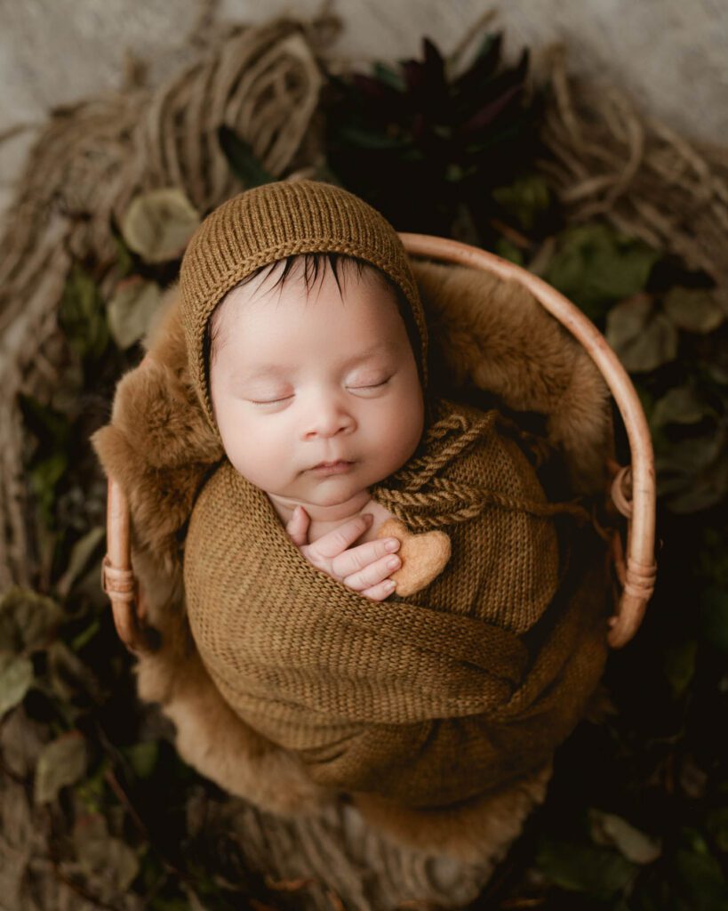 Dallas Newborn Photographer With A Peacefully Sleeping Newborn Wrapped In A Warm Neutral Knit Wrap Inside A Rustic Basket During A Professional Studio Newborn Photography Session.