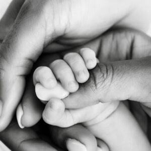 Close-up black and white portrait of a newborn baby's tiny hand holding a parent's finger during a Dallas newborn photography session.