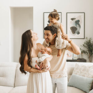 Parents holding their newborn while their toddler sits on dad's shoulders during a lifestyle newborn photography session in the Dallas area.