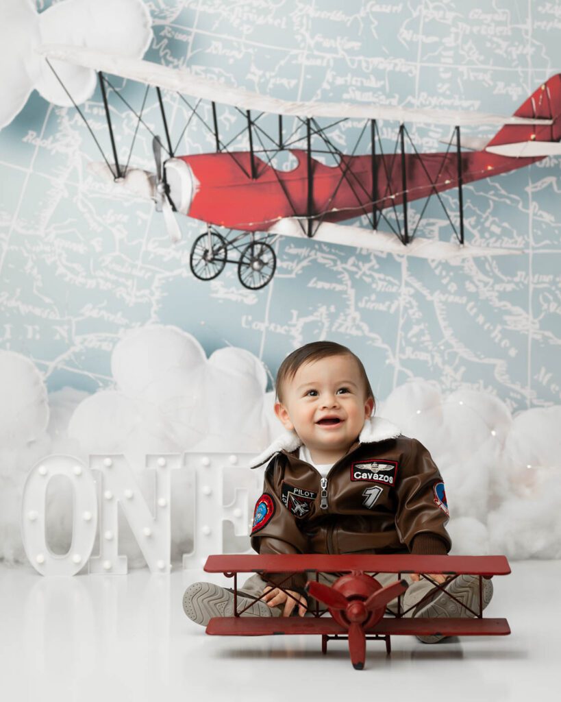 Baby Sitting Beside A Vintage Airplane Prop During A First Birthday Session With Dallas Baby Photographer