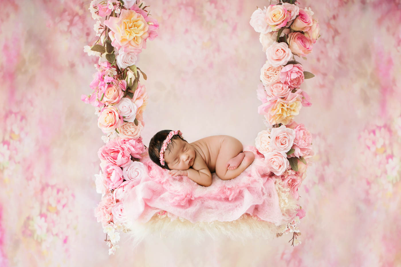Baby girl newborn photography in Dallas featuring a sleeping newborn posed on a floral swing surrounded by soft pink flowers