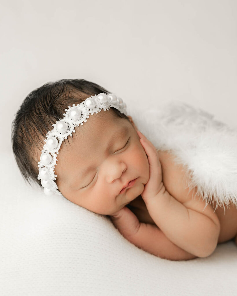 Popular Newborn Photography Styles In Dallas 12 Sleeping Newborn Baby Girl Wearing A White Floral Headband During A Studio Newborn Photography Session In Dallas, Texas.