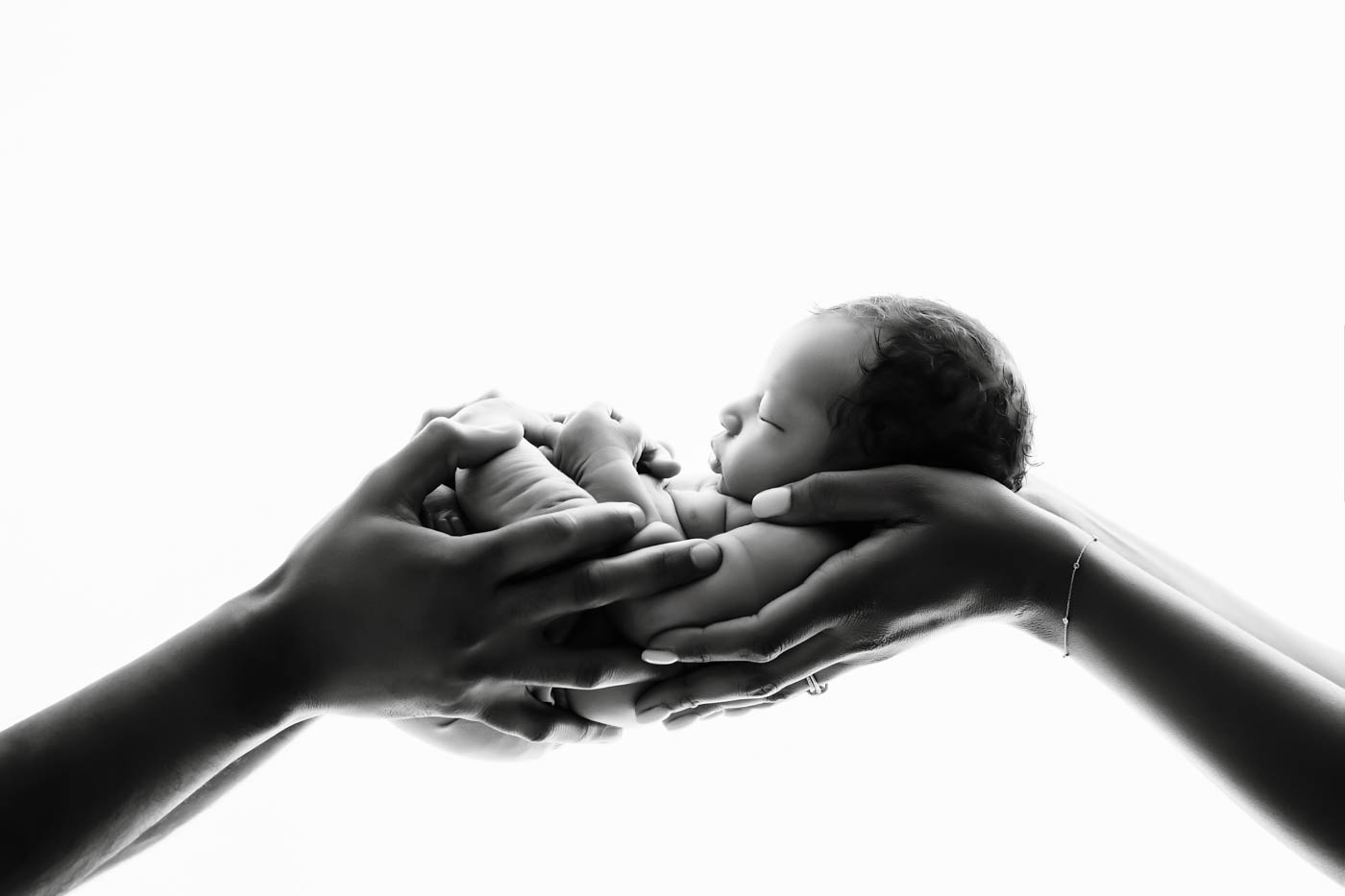 Black and white newborn portrait featuring a sleeping baby cradled in the hands of loving parents during a Dallas newborn photography session