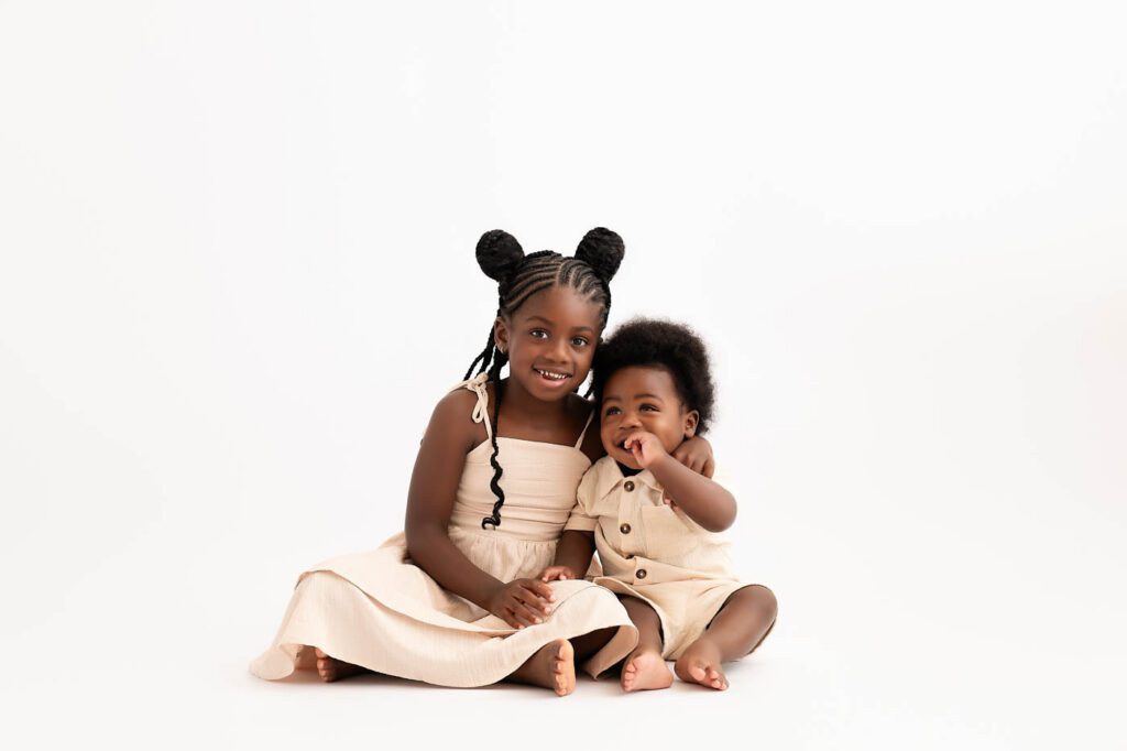 Older Sister Sitting With Her Baby Brother During A First Birthday Photography Session In Dallas.
