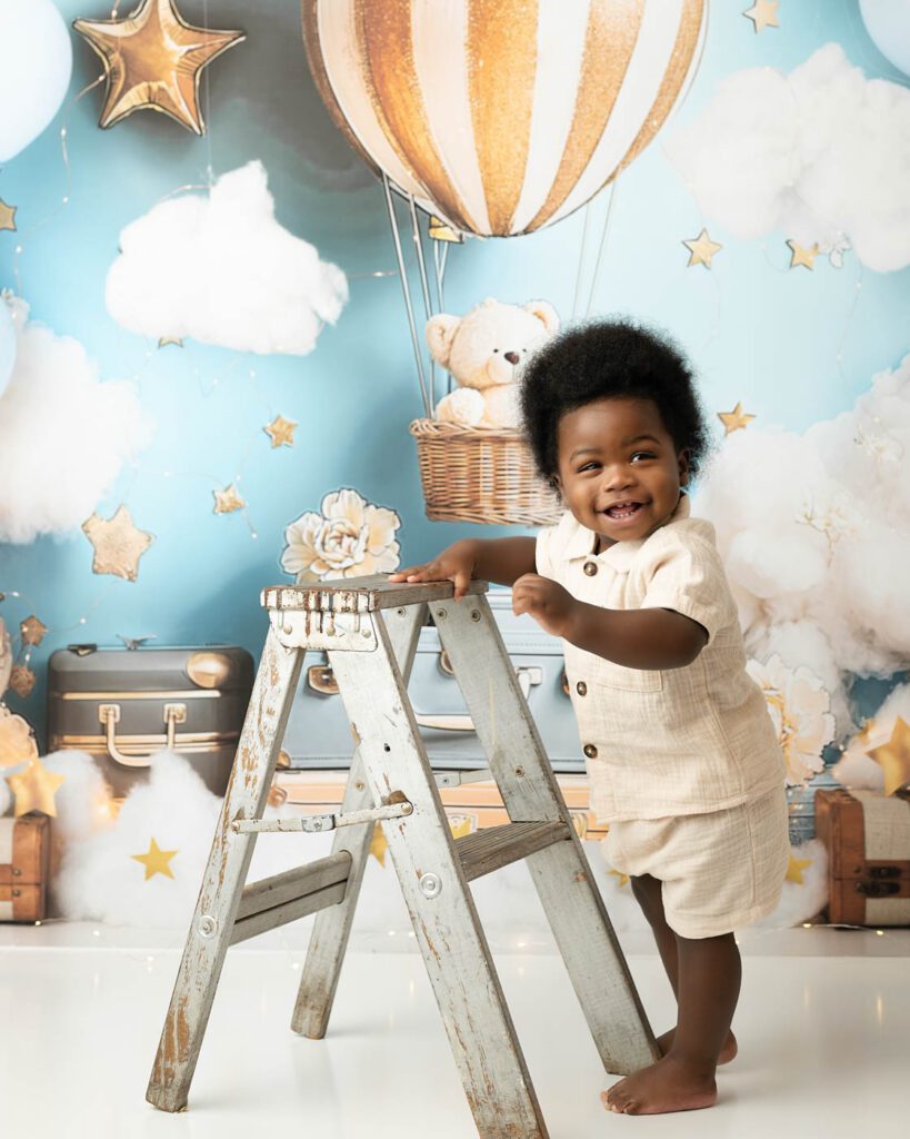One-Year-Old Standing Beside A Ladder During A Hot Air Balloon Cake Smash Session In Dallas.