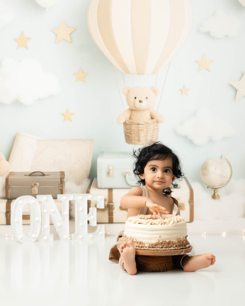 What If Your Baby Won’t Smash The Cake During A Cake Smash Session? 13 Baby Exploring Cake Before The Smash During A Dallas Cake Smash Photography Session As She Carefully Reaches Toward The Birthday Cake For The First Time.
