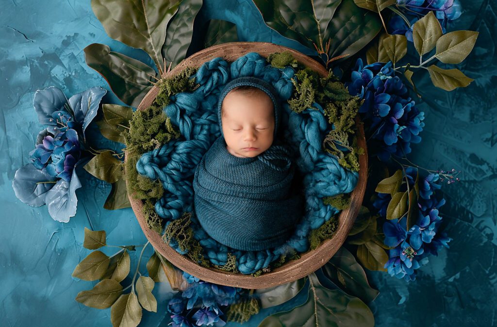The Role Of A Dallas Newborn Photographer Before, During, And After Your Session 10 Wrapped Newborn Sleeping In A Wooden Bowl Surrounded By Rich Blue Flowers During A Dallas Newborn Photography Studio Session.