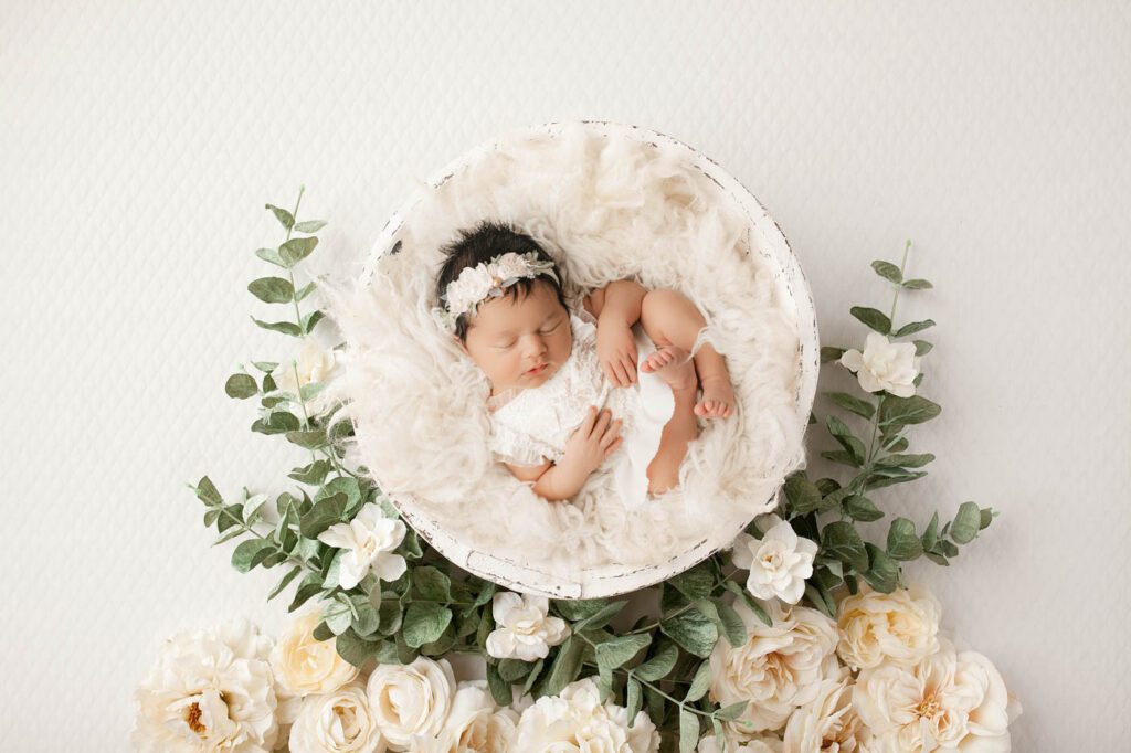 Sleeping Newborn In A White Basket Surrounded By Elegant White Flowers During A Dallas Newborn Photography Studio Session.