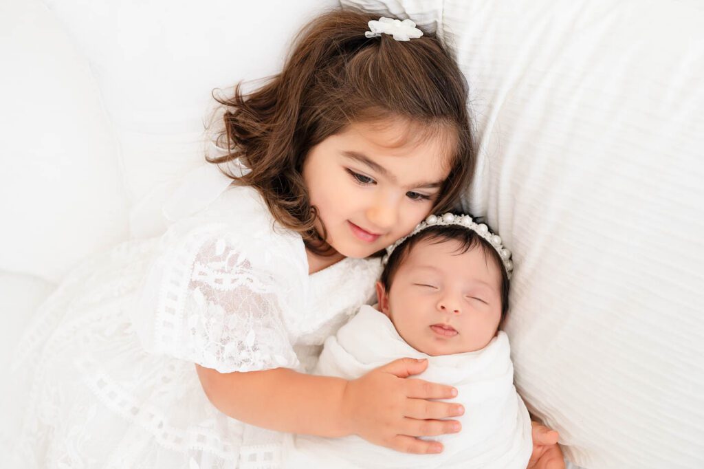 Big Sister Cuddling Her Newborn Baby Sibling During A Newborn Photography Session With A Newborn Photographer In Dallas.