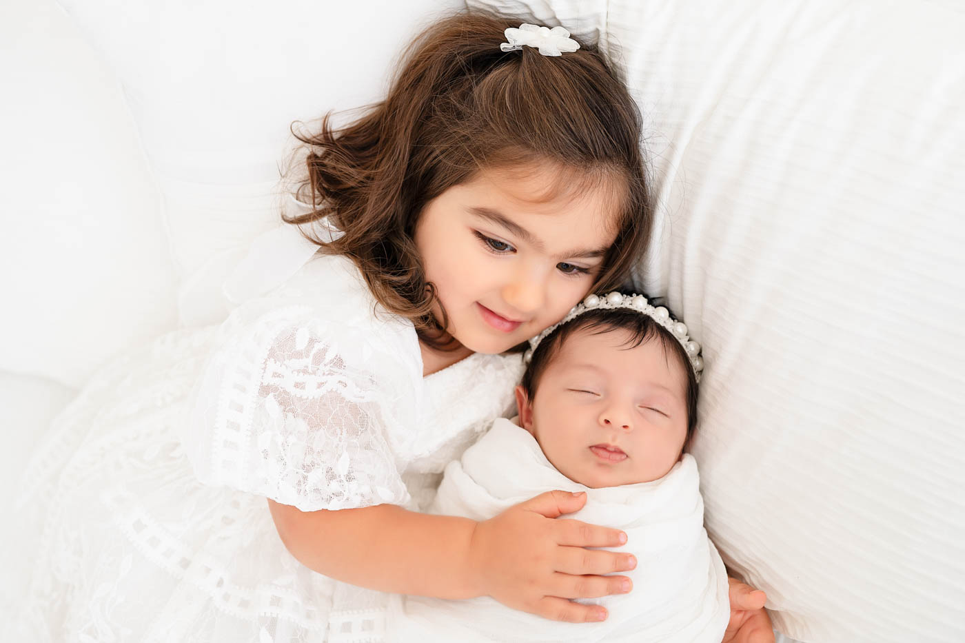 Big sister cuddling her newborn baby sibling during a newborn photography session with a newborn photographer in Dallas.