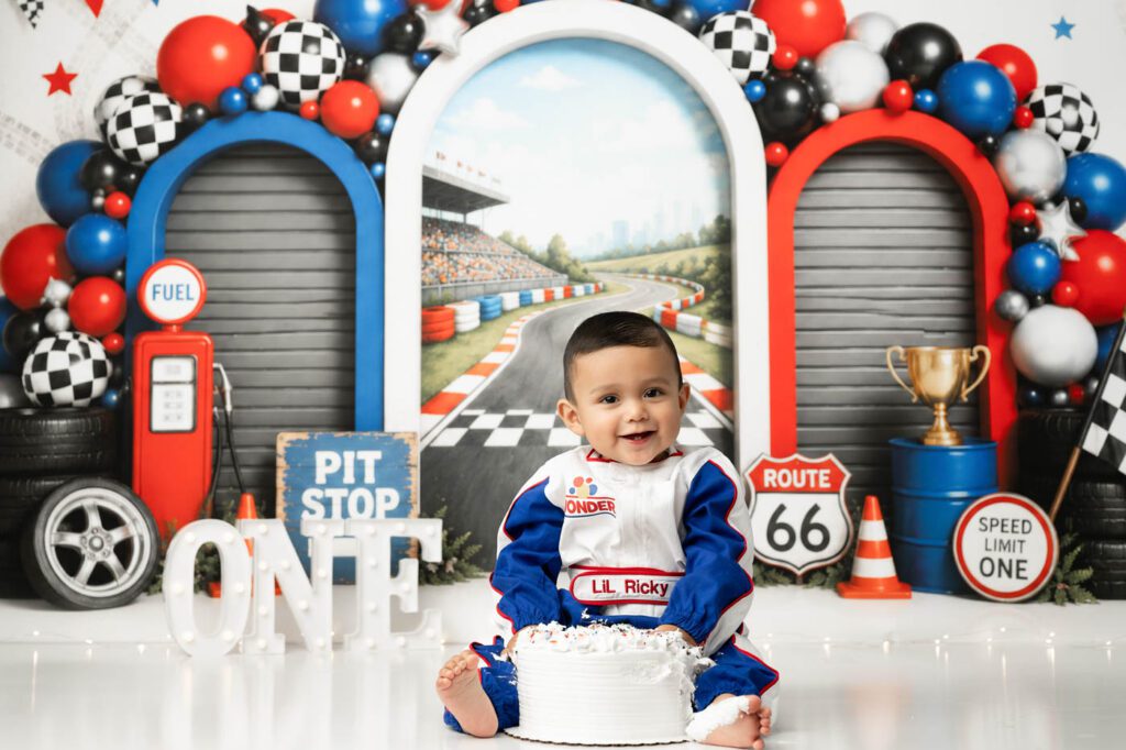 One-Year-Old Boy Dressed As A Race Car Driver During A Race Car Themed Cake Smash Photography Session In Dallas, Texas.